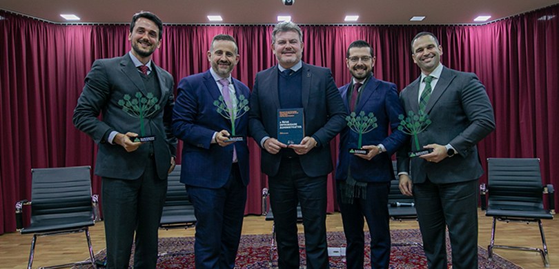 Foto em que aparecem cinco homens em pé posando para a foto sobre o palco do auditório do TRE-PR...