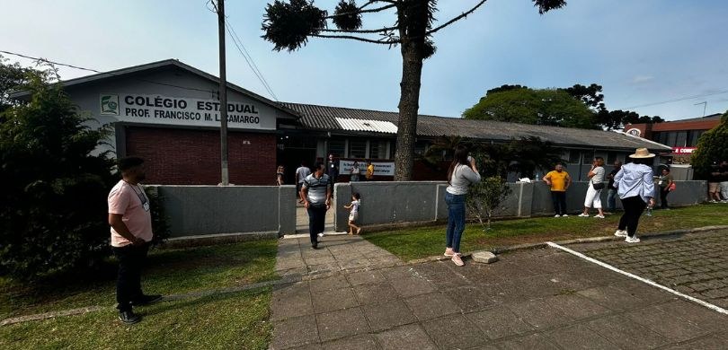 Foto em que aparecem pessoas em frente a uma escola, que é local de votação em São José dos Pinh...