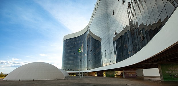 Fotografia da fachada do TSE, que é predominantemente preta, envidraçada, em sua forma sinuosa. ...