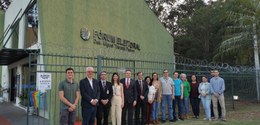 Fotografia de 15 pessoas, entre homens e mulheres, posando sorrindo em frente ao Fórum Eleitoral...