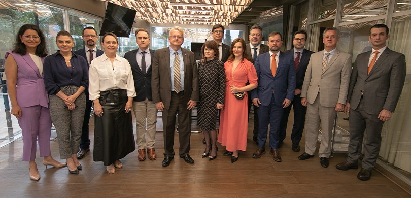 Fotografia de 14 pessoas, entre homens e mulheres, posando sorrindo. Os homens vestem terno e as...