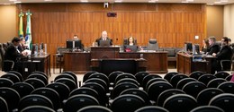 Fotografia da sala de sessões, em que os membros da Corte aparecem sentados diante de três mesas...