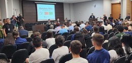 Em uma sala com paredes brancas, encontra-se, centralizado, um painel de madeira, em frente ao q...