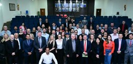 Fotografia de várias pessoas, entre homens e mulheres, posando sorrindo em pé em um auditório. A...