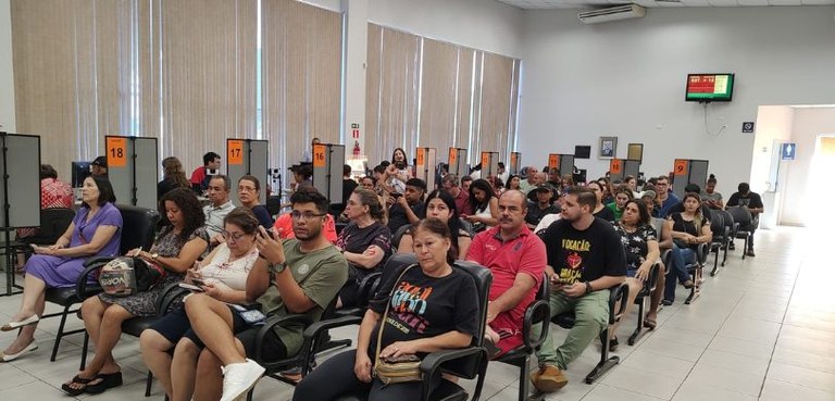 Fórum Eleitoral de Maringá. Várias pessoas estão sentadas aguardando atendimento em cadeiras pre...