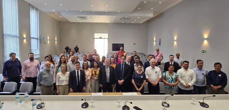 Fotografia de diversas pessoas, entre homens e mulheres, posando sorrindo em pé em um auditório ...