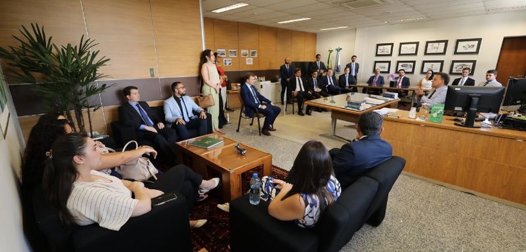 Fotografia de homens e mulheres em uma sala com paredes trabalhadas em madeira e carpete cinza. ...