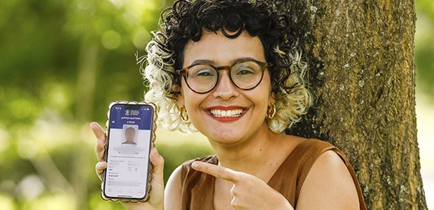 Fotografia de uma mulher sorrindo apontando o dedo indicador da mão esquerda para um smartphone,...