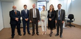 Foto em que aparecem duas mulheres e quatro homens em pé, posando. Entre eles, que usam ternos e...