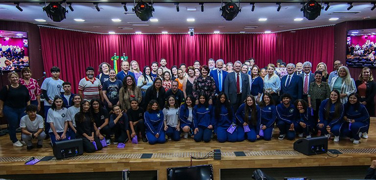 Foto em que aparecem vários estudantes entre algumas autoridades posando sobre o palco do auditó...