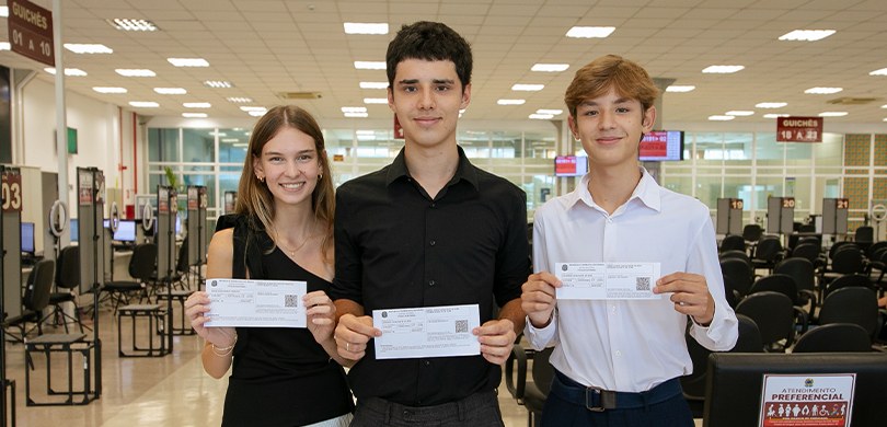 Foto em que aparecem três jovens, uma garota e dois garotos, segurando o Título de Eleitor dentr...