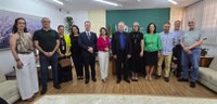 Fotografia de seis mulheres e seis homens posando sorrindo lado a lado. A sala tem paredes branc...