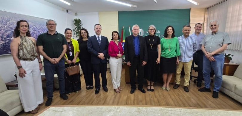 Fotografia de seis mulheres e seis homens posando sorrindo lado a lado. A sala tem paredes branc...