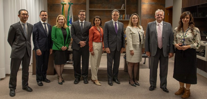 Fotografia de quatro mulheres, que vestem roupas formais, e cinco homens de terno posando sorrin...