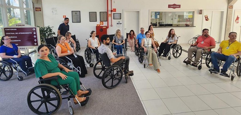 Homens e mulheres sentados em cadeiras de rodas formam um semicírculo em um hall de entrada. Ao ...