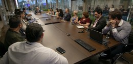 Fotografia de diversas pessoas, entre homens e mulheres, ao redor de uma mesa de reunião em made...