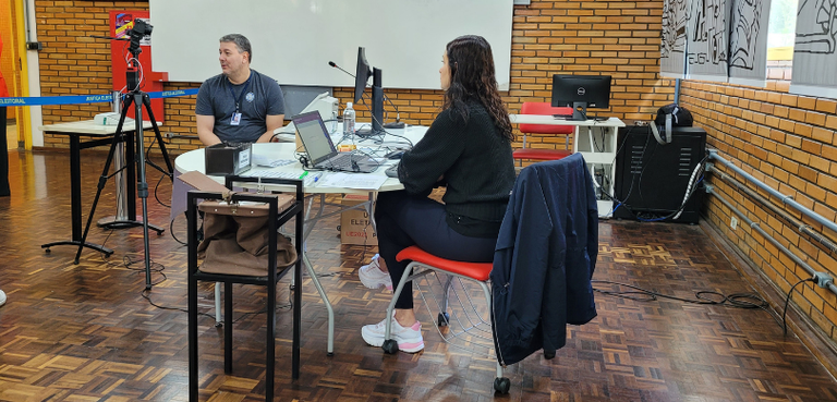 Fotografia de uma mulher sentada em uma cadeira de estofado vermelho de frente para uma mesa bra...