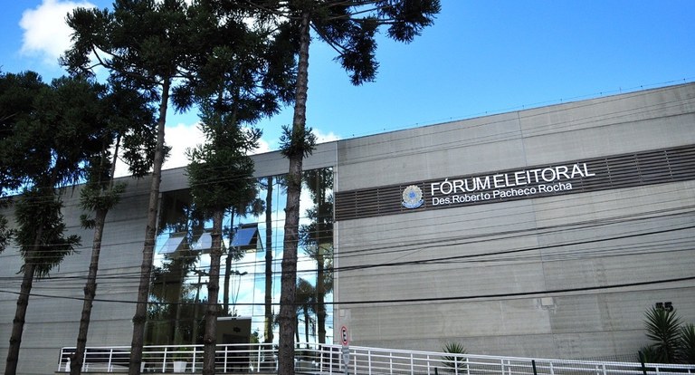 Foto da fachada do Fórum Eleitoral de Curitiba. Na fachada do prédio em concreto lê-se em um pai...