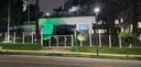 Fotografia da fachada do edifício-sede do TRE-PR iluminada na cor verde, durante a noite. Ao red...