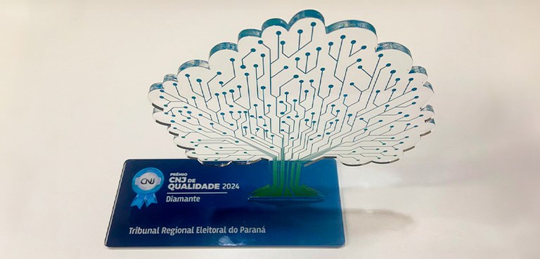 Foto em que aparece o troféu recebido pelo TRE-PR representando o Selo Diamante. O objeto consis...