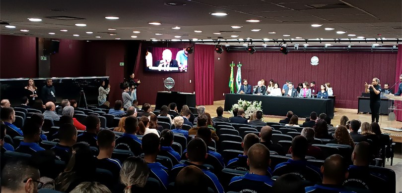 Foto em que aparece o auditório do TRE-PR. Veem-se várias pessoas sentadas de costas em poltrona...