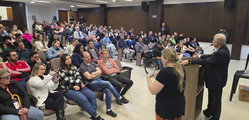 Foto em que aparecem, do lado esquerdo, um homem de terno falando em um púlpito de madeira, e um...