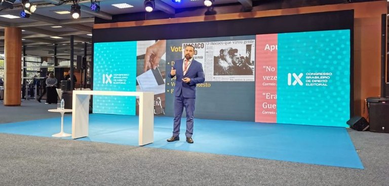 Foto em que aparece o secretário de TI, Gilmar de Deus, falando em pé à frente de um painel colo...