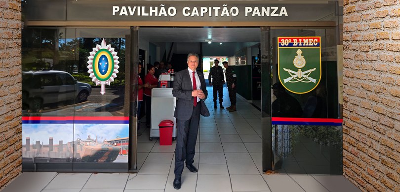 Foto em que aparece o des. Panza em pé, na porta de entrada do Pavilhão Capitão Panza. Dos lados...