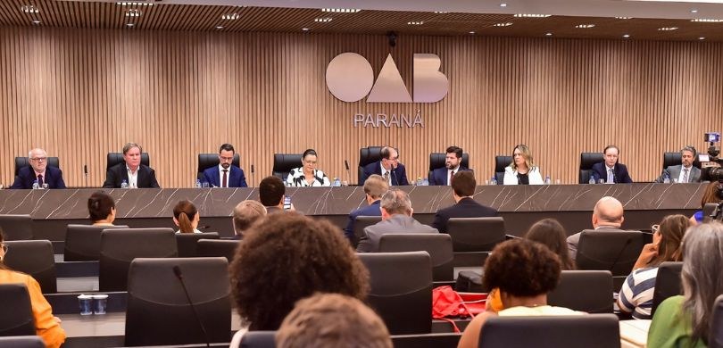 Fotografia de diversas pessoas, entre homens e mulheres, sentadas em cadeiras de estofado preto,...